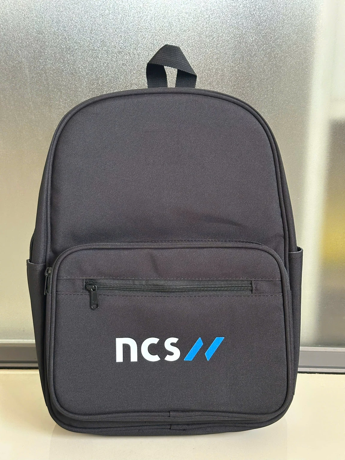 Ba lô xám đậm với ngăn khóa phía trước và phần in ncs xanh trắng