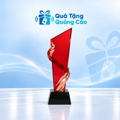 Minh họa biểu trưng pha lê K9 thân vát chéo mảng đỏ, chi tiết uốn ánh đồng và đế đen trên nền xanh