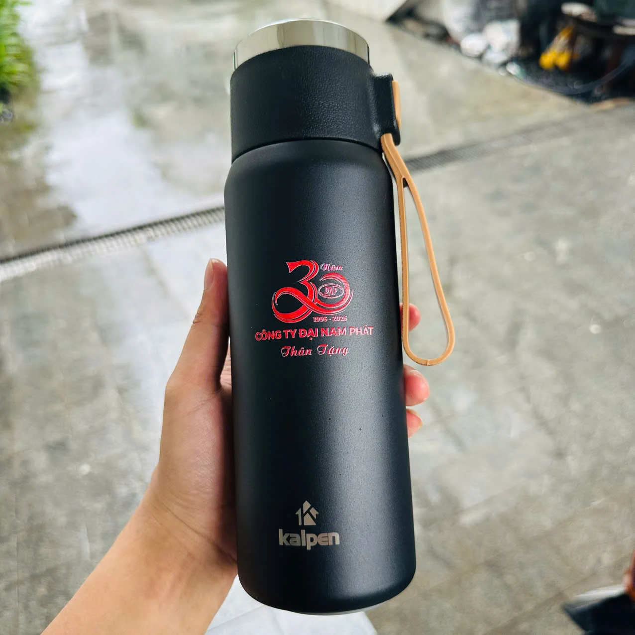 Bình đen có dây cầm màu vàng nâu và phần in kỷ niệm nguồn, nhãn Kalpen ở chân