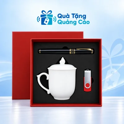 Minh họa đủ ba món trong hộp đỏ khay đen: bút ngang phía trên, cốc trắng có nắp hình ngọn lửa bên trái và USB đỏ vỏ bạc bên phải
