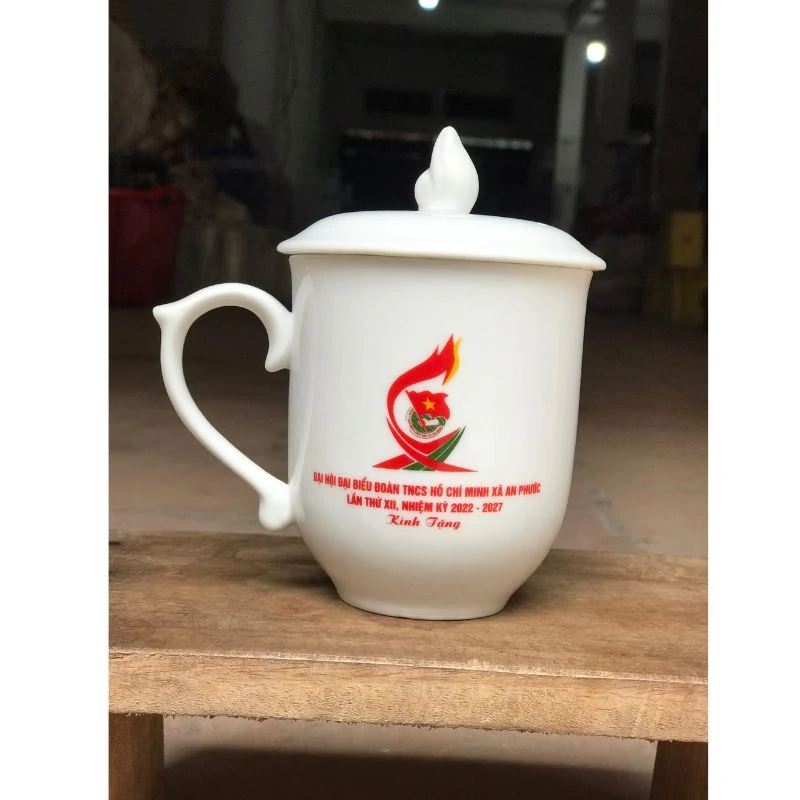 Tư liệu cốc sứ trắng có quai uốn lượn, nắp có núm hình ngọn lửa và nhận diện tham khảo trên mặt trước