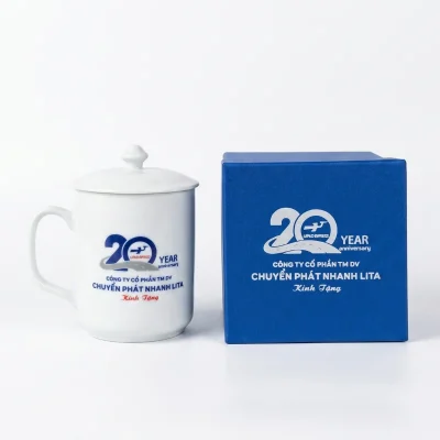 Tư liệu cốc sứ trắng quai vuông đóng nắp, bên cạnh hộp đơn cốc màu xanh và nhận diện tham khảo