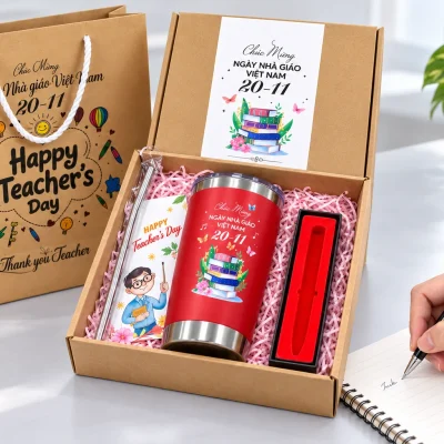 Minh họa một bàn tay dùng bút đen ghi chép cạnh bộ quà, hộp bút lót đỏ đã trống và ly vẫn trong hộp