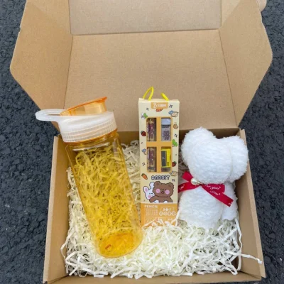 Ảnh tư liệu hộp carton mở với bình nhựa vàng, bộ bút chì tẩy gọt và khăn gấu trắng