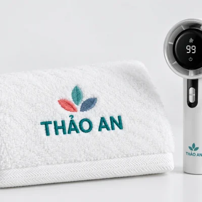 Minh họa nhận diện THẢO AN thêu ba màu trên khăn trắng và in một màu trên thân quạt mini