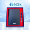 Minh họa sổ xanh đen và bút kim loại xanh nằm trong hộp viền xanh khay đỏ trên nền thương hiệu