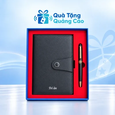 Minh họa sổ đen tai gài mặt tròn và bút đen phối vàng nằm trong hộp viền xanh khay đỏ trên nền thương hiệu