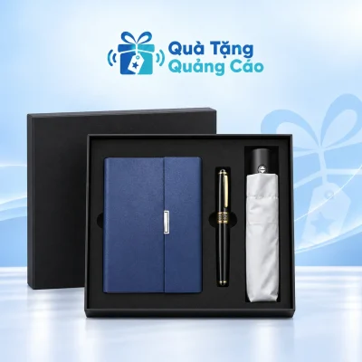 Minh họa đủ ba món trong hộp đen: sổ SC08 xanh bên trái, bút đen viền vàng ở giữa và dù trắng gấp gọn bên phải