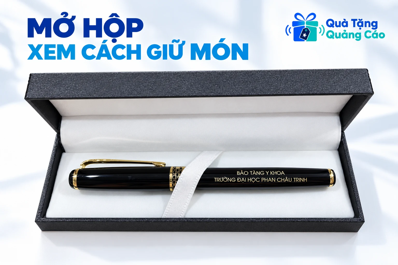 Bút đen viền vàng nằm trong hộp đen mở có lớp lót trắng và dây giữ theo ảnh nguồn