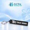 Móc khóa cao su đen bản dài có dây xích, khoen tròn và chữ nổi TRUC MINH trên nền Quà Tặng Quảng Cáo