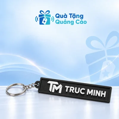 Móc khóa cao su đen bản dài có dây xích, khoen tròn và chữ nổi TRUC MINH trên nền Quà Tặng Quảng Cáo