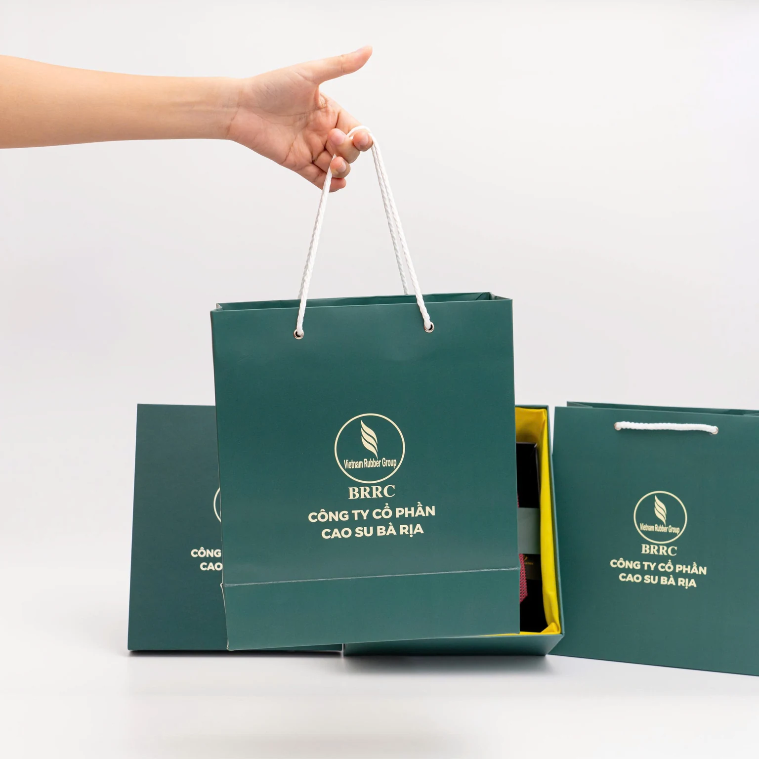 Túi và hộp xanh BRRC có quai trắng, giữ phần in nguồn và lớp lót vàng đang thấy