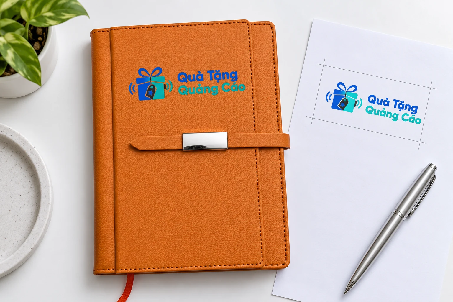 Logo Quà Tặng Quảng Cáo minh họa trên phần bìa cam phía trên đai, cạnh bản bố trí trên giấy